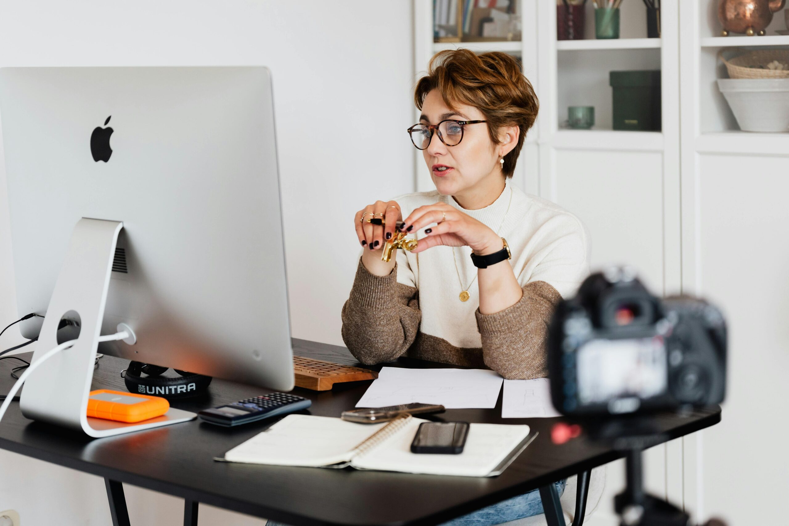 A professional woman engaged in a virtual meeting setup at her home desk, using a computer and camera. Live training session about the harsh reality of online business and how to overcome common struggles.